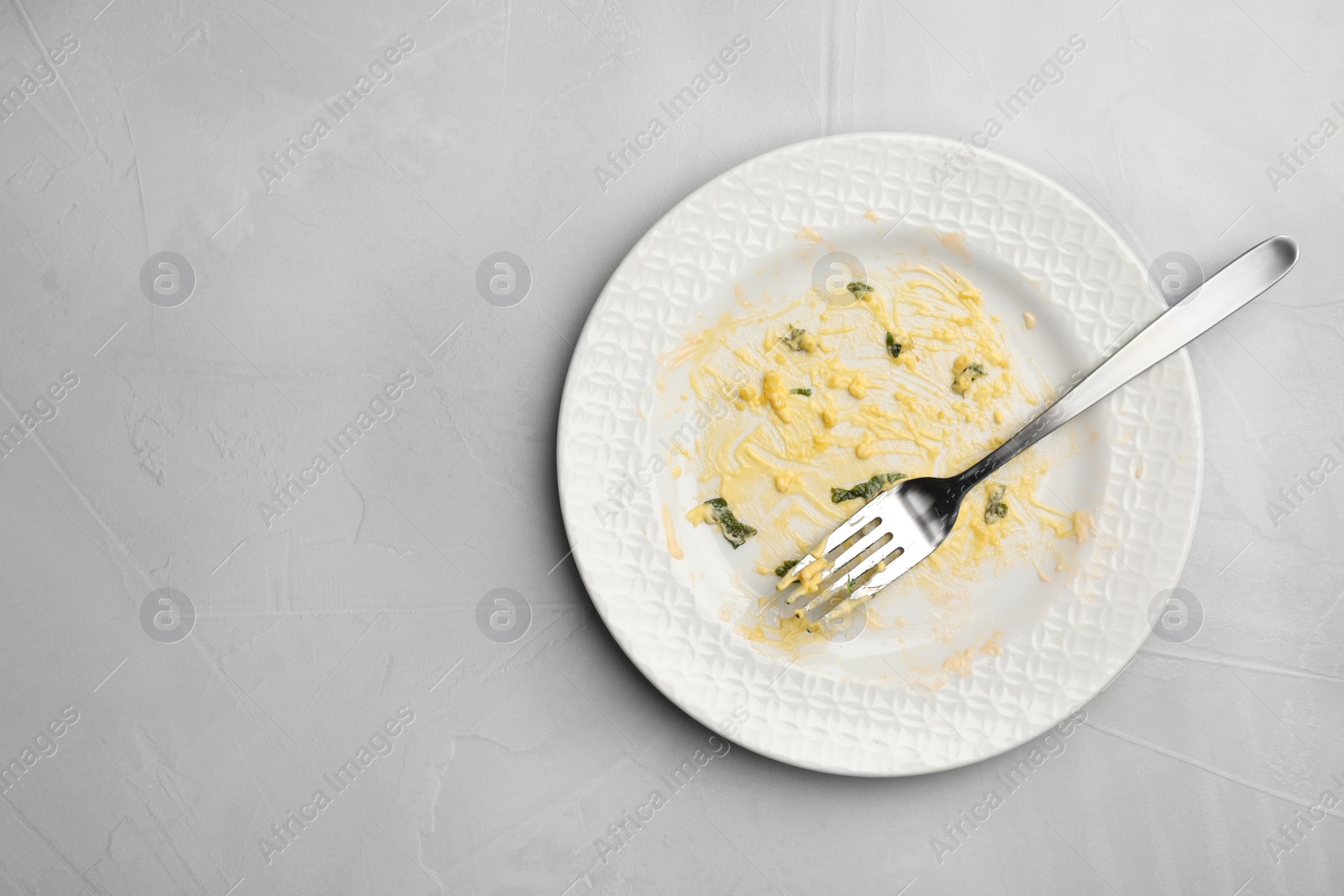 Photo of Dirty plate with food leftovers and fork on grey background, top view. Space for text