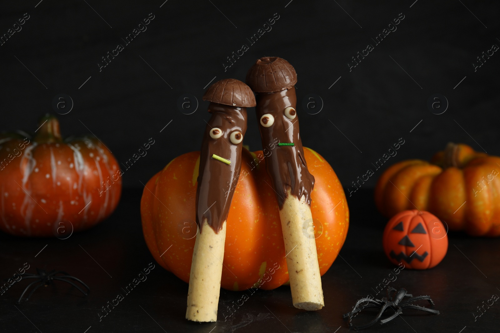 Photo of Delicious sticks with chocolate decorated as monsters on dark background. Halloween treat