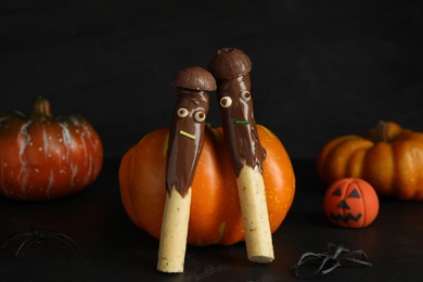 Photo of Delicious sticks with chocolate decorated as monsters on dark background. Halloween treat