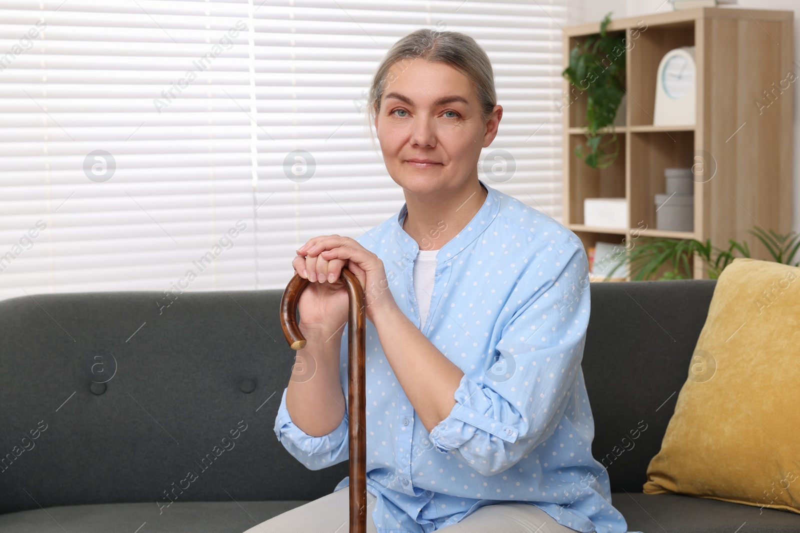 Photo of Senior woman with walking cane sitting on sofa at home. Space for text