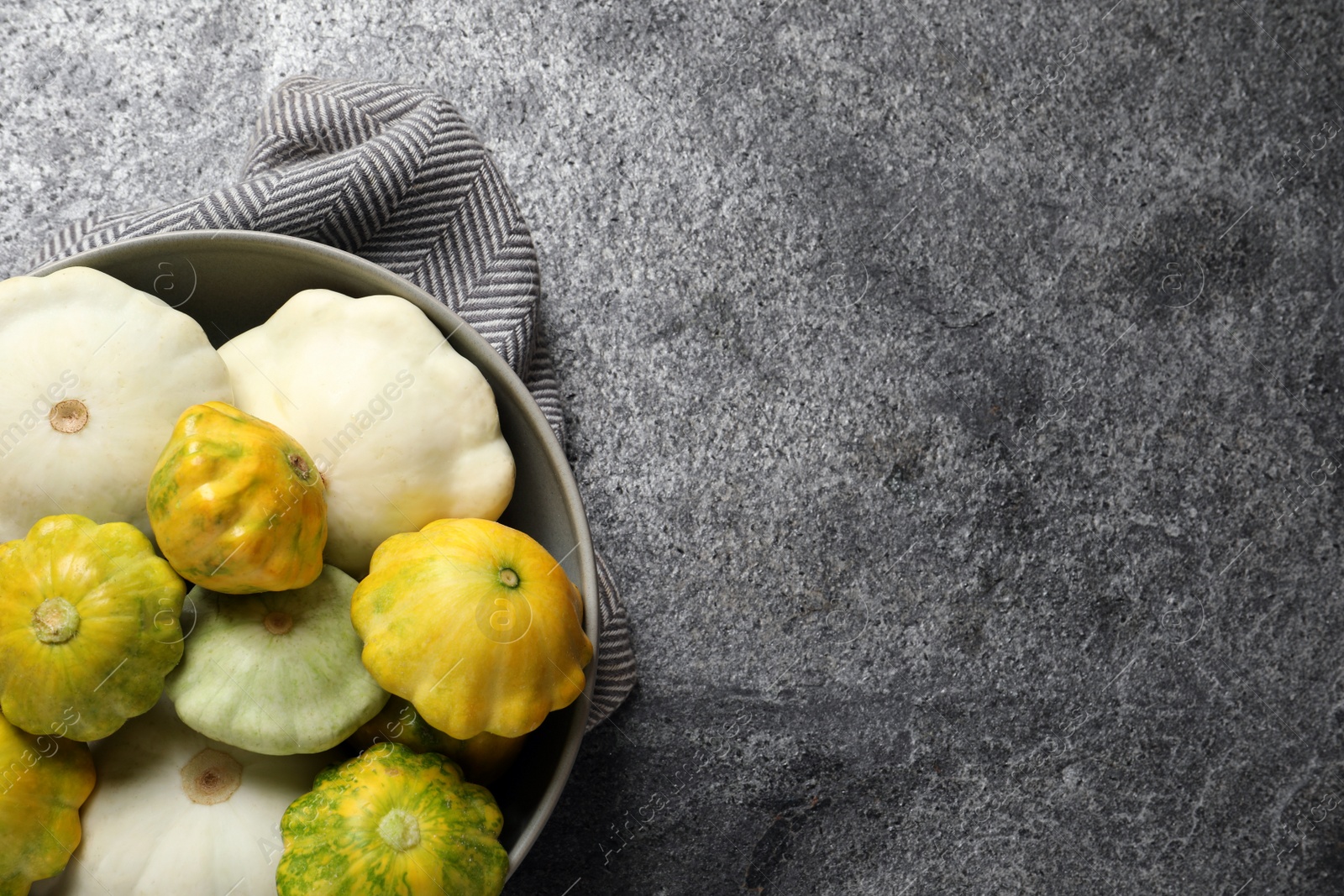 Photo of Fresh ripe pattypan squashes in bowl on grey table, top view. Space for text
