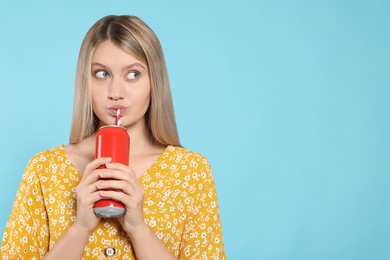 Beautiful woman drinking from red beverage can on light blue background. Space for text