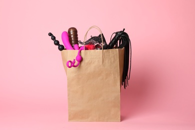 Photo of Paper shopping bag with different sex toys on pink background