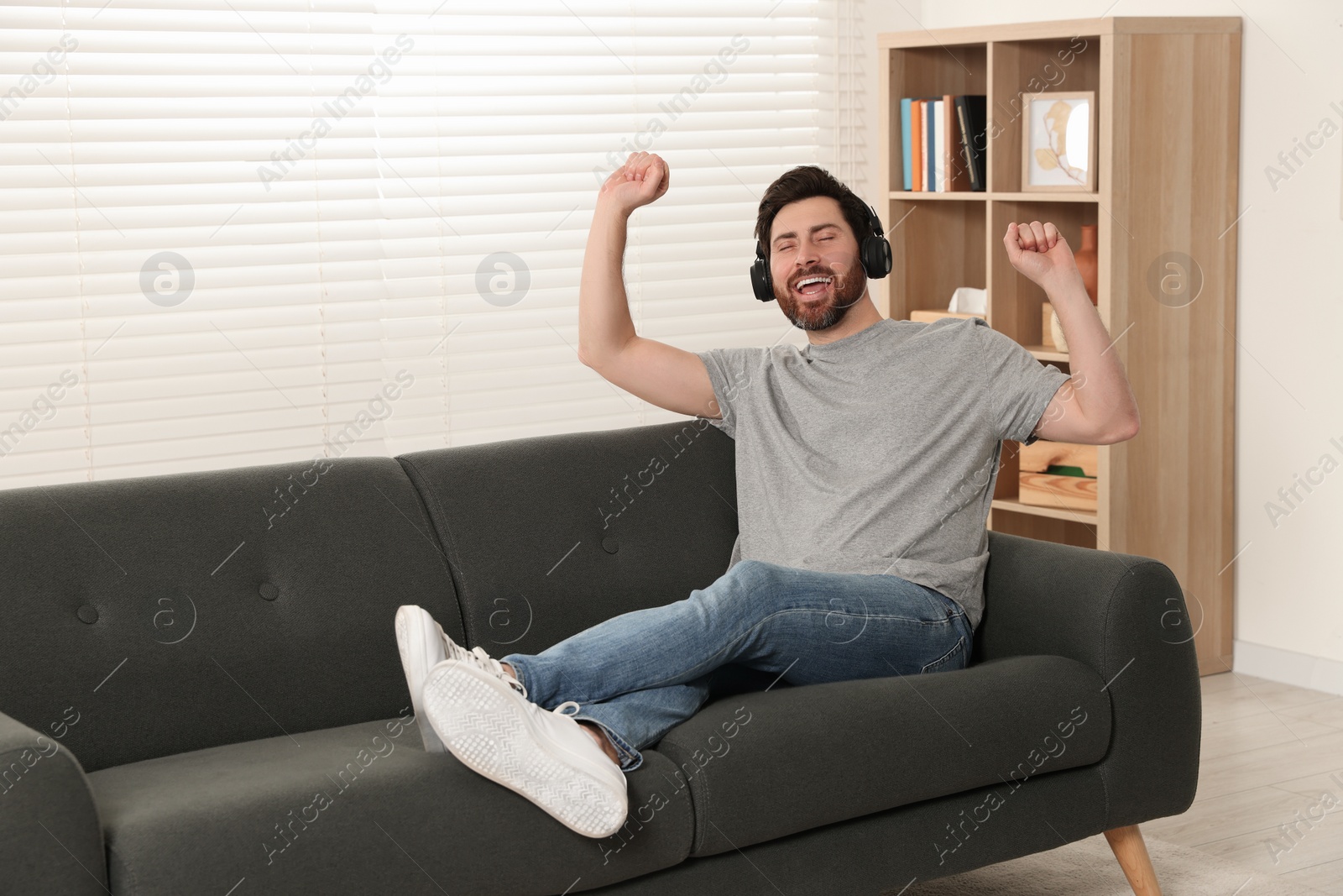 Photo of Handsome man listening music with headphones on sofa indoors. Space for text