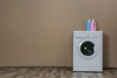 Modern washing machine with detergents near beige wall, space for text. Laundry day