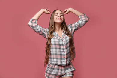 Photo of Beautiful woman in pajamas stretching on dusty rose background. Bedtime