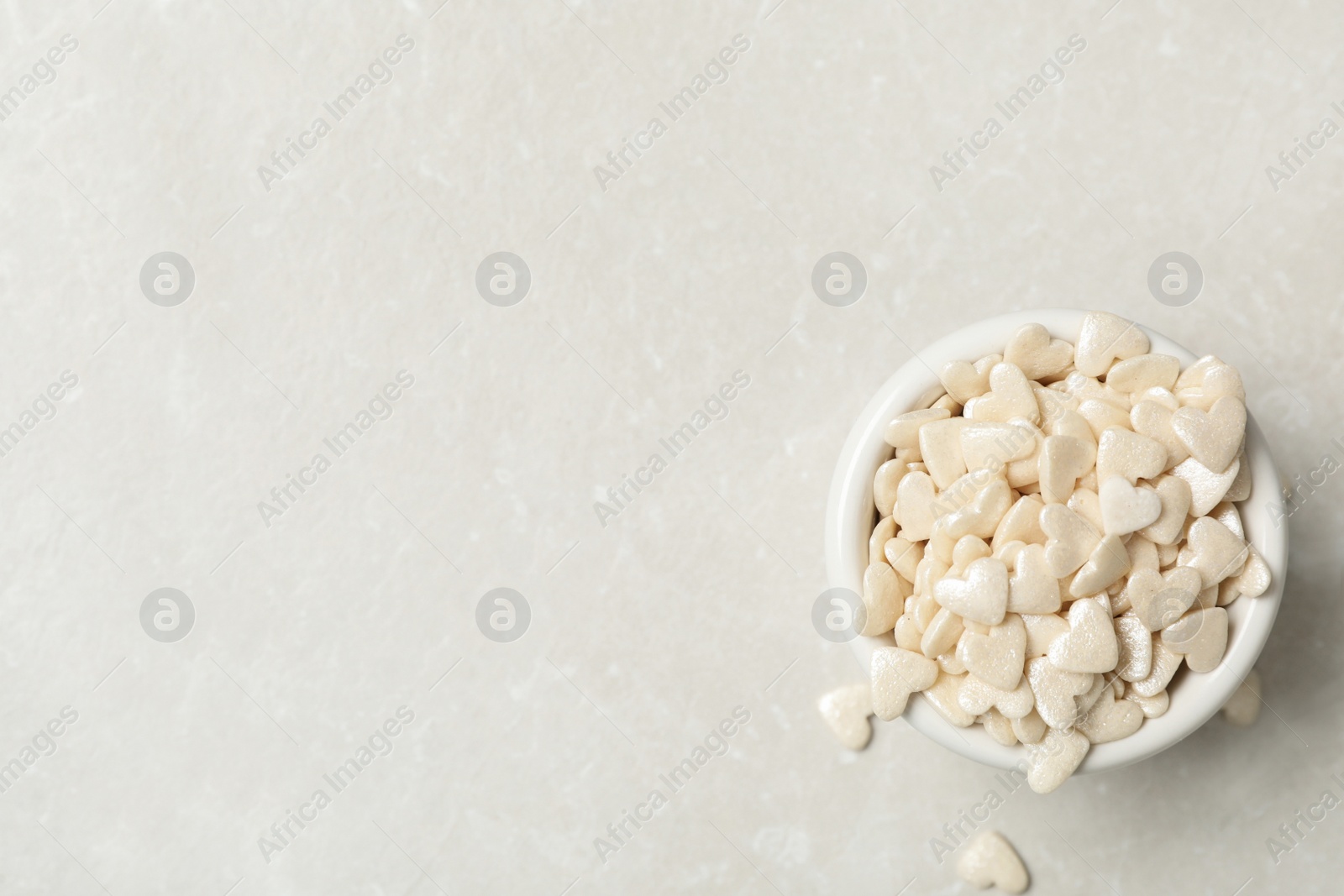 Photo of White heart shaped sprinkles in bowl on light grey table, flat lay. Space for text