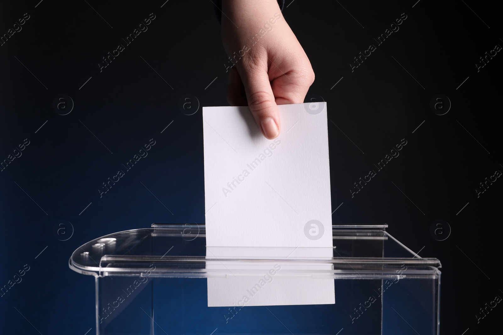 Photo of Woman putting her vote into ballot box on dark blue background, closeup