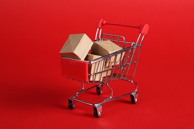 Small metal shopping cart with cardboard boxes on red background