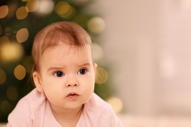 Portrait of cute little baby against blurred festive lights, space for text. Winter holiday