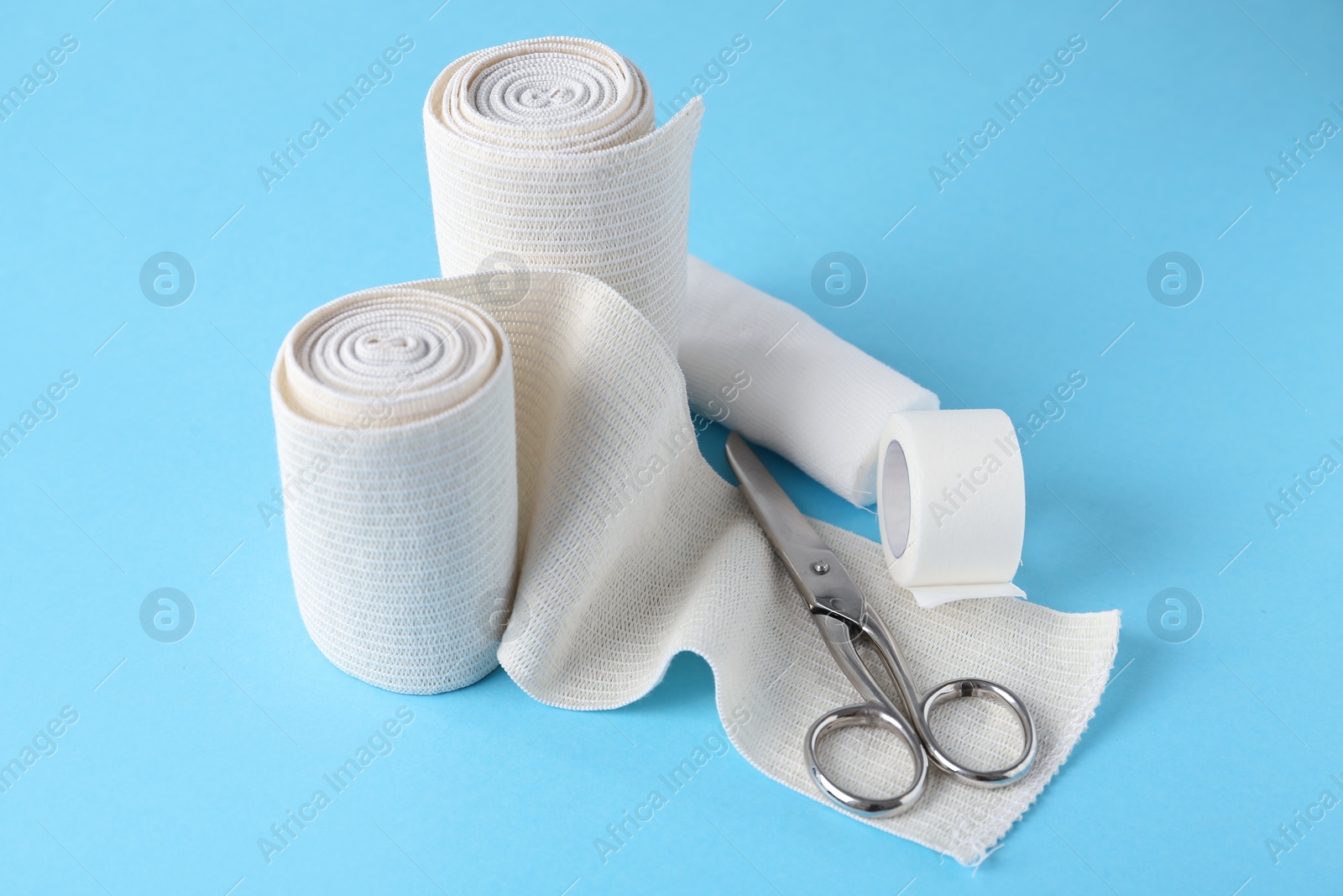 Photo of Medical bandage rolls, sticking plaster and scissors on light blue background