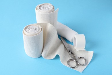 Photo of Medical bandage rolls, sticking plaster and scissors on light blue background