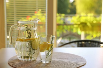 Photo of Jug and glass with refreshing lemon water on light table indoors. Space for text