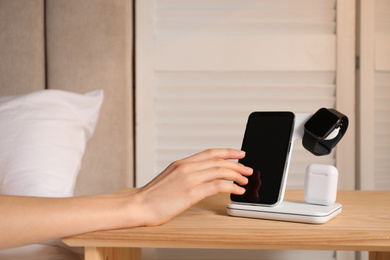 Woman taking smartphone from wireless charger in bedroom, closeup