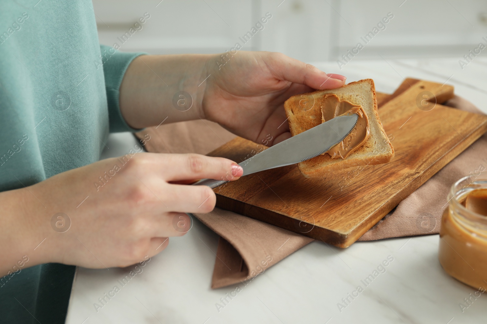 Photo of Woman spreading tasty nut butter onto toast at white table, closeup