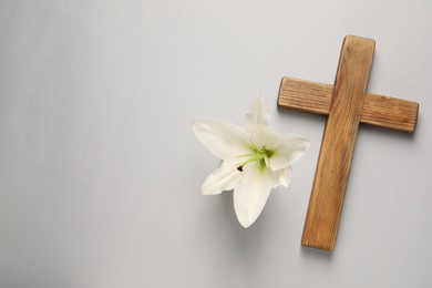 Photo of Wooden cross and lily flower on grey background, top view with space for text. Easter attributes