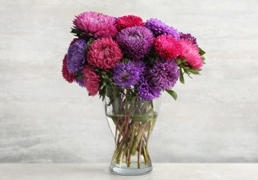 Photo of Beautiful asters in vase on table against white background. Autumn flowers