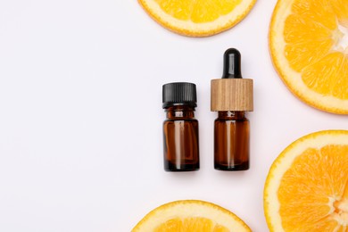 Photo of Bottles of citrus essential oil and fresh orange slices on white background, flat lay. Space for text