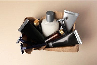Box with different men's shaving accessories and cosmetics on beige background, top view