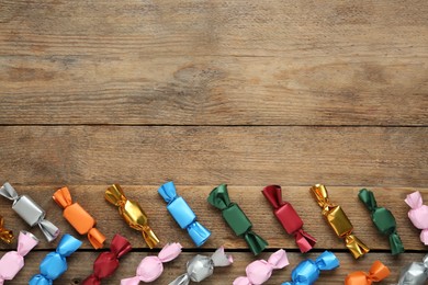 Photo of Candies in colorful wrappers on wooden table, flat lay. Space for text