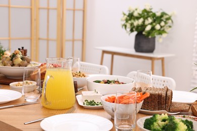 Photo of Healthy vegetarian food, jug of juice, cutlery, glasses and plates on wooden table indoors