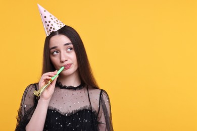 Photo of Woman in party hat with blower on orange background, space for text