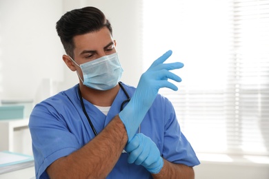 Photo of Doctor in protective mask putting on medical gloves indoors