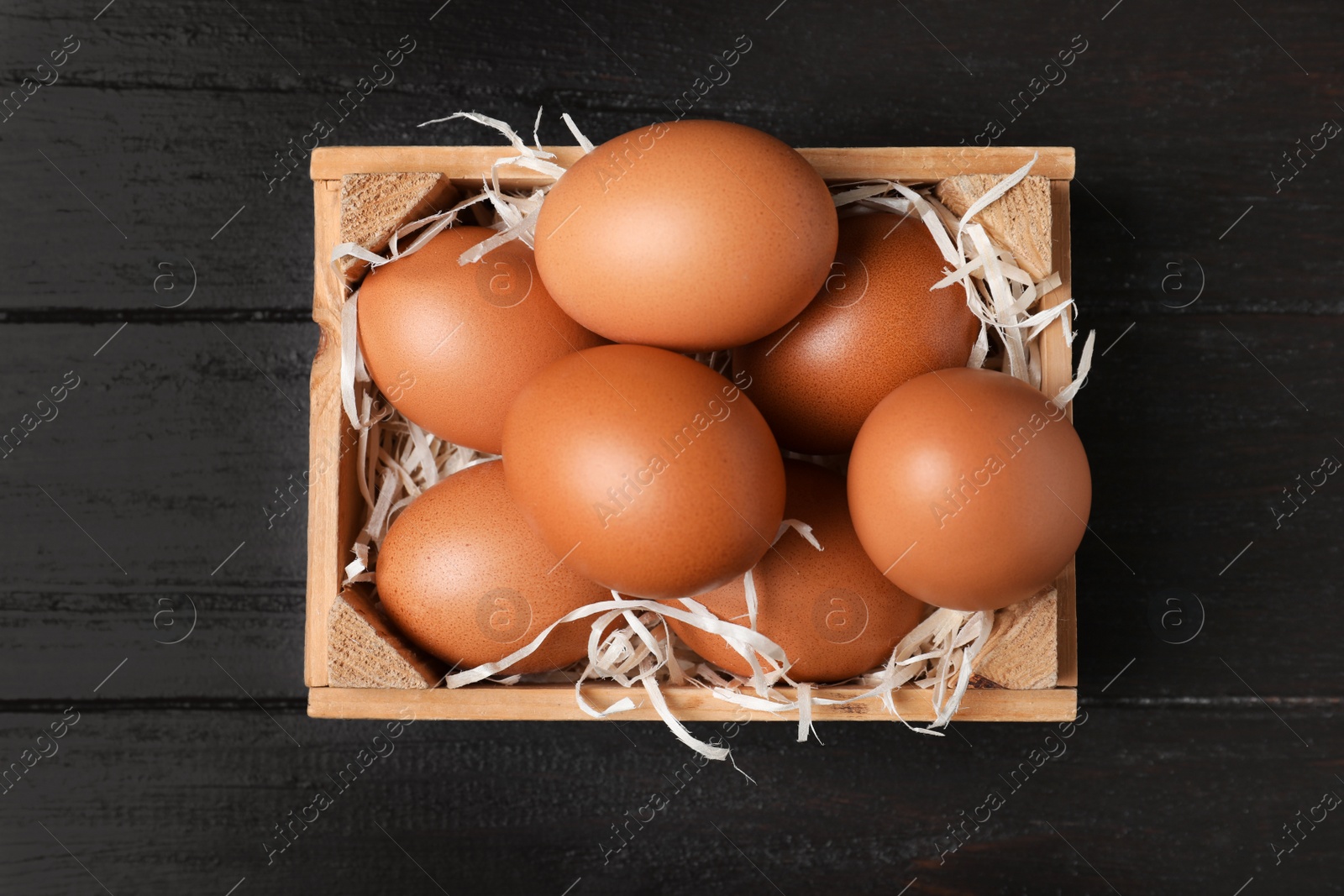 Photo of Wooden crate full of fresh eggs on dark background, top view