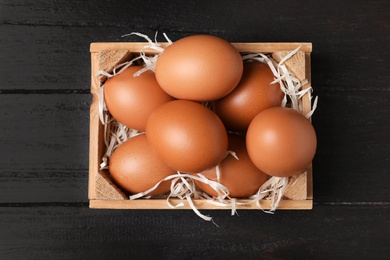 Wooden crate full of fresh eggs on dark background, top view