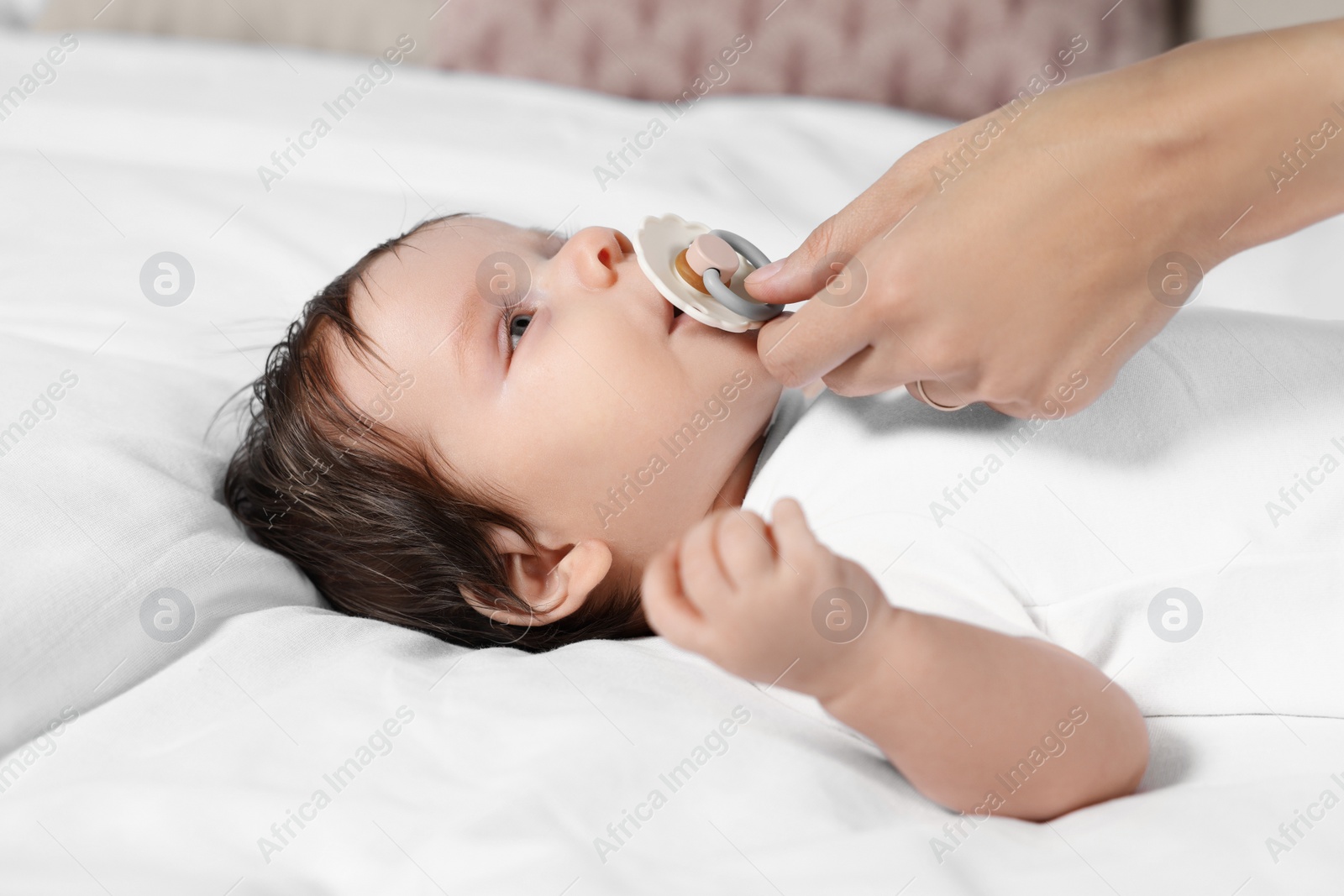 Photo of Mother giving pacifier to her little baby on bed, closeup