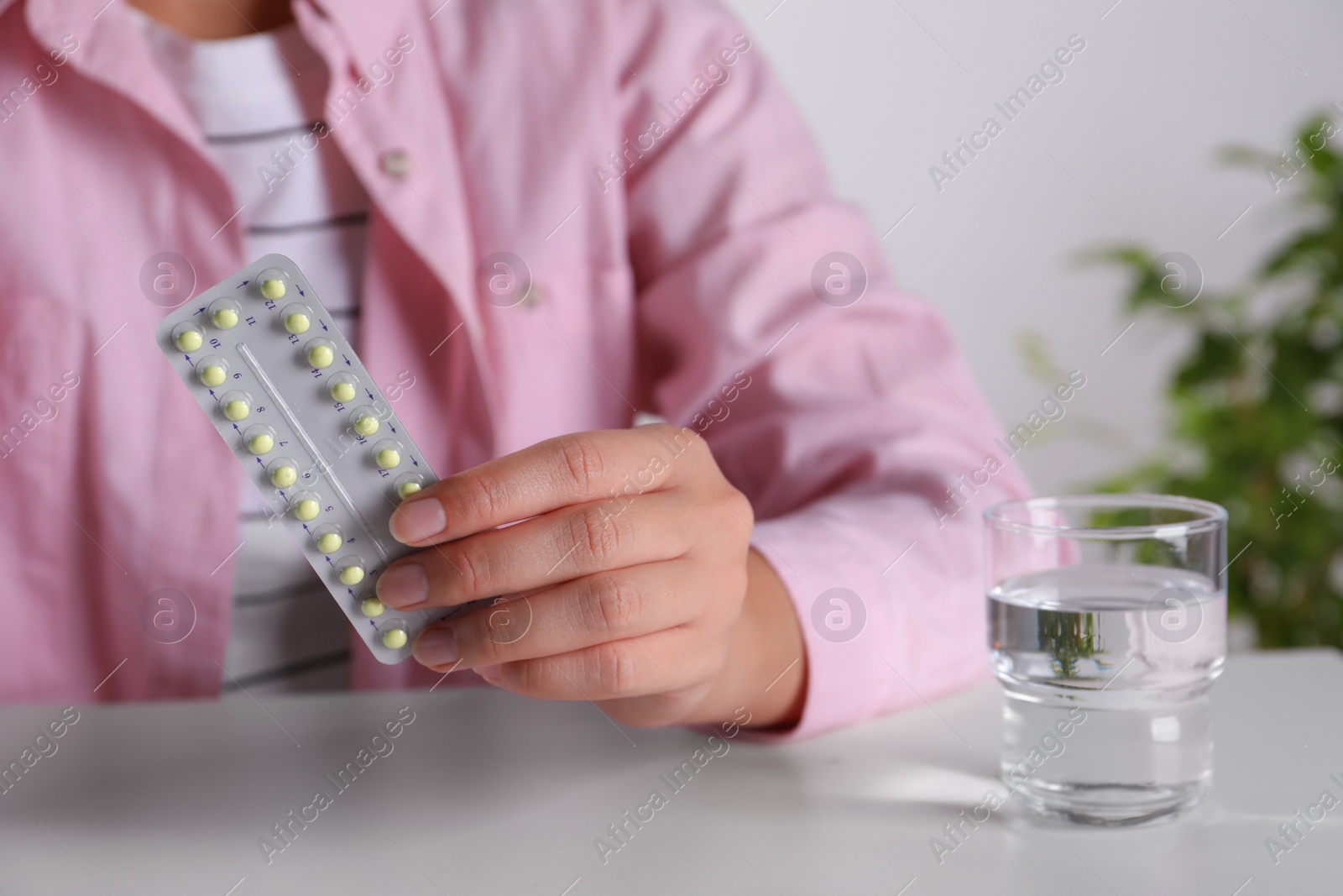 Photo of Woman holding blister of oral contraceptive pills at white table, closeup