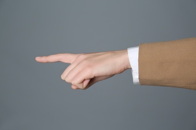 Photo of Businesswoman pointing at something on grey background, closeup. Finger gesture