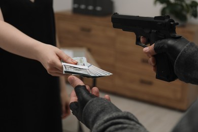 Woman giving money to criminal with gun indoors, closeup. Armed robbery
