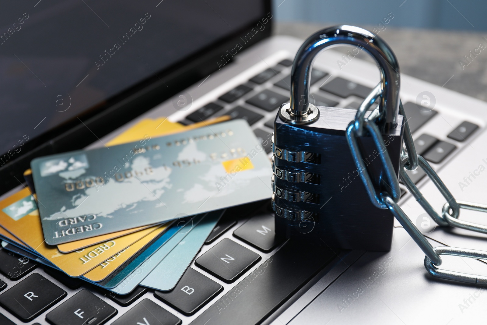 Photo of Cyber security. Metal combination padlock with chain and credit cards on laptop, closeup