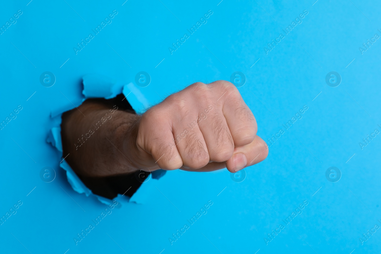 Photo of Man breaking through light blue paper with fist, closeup