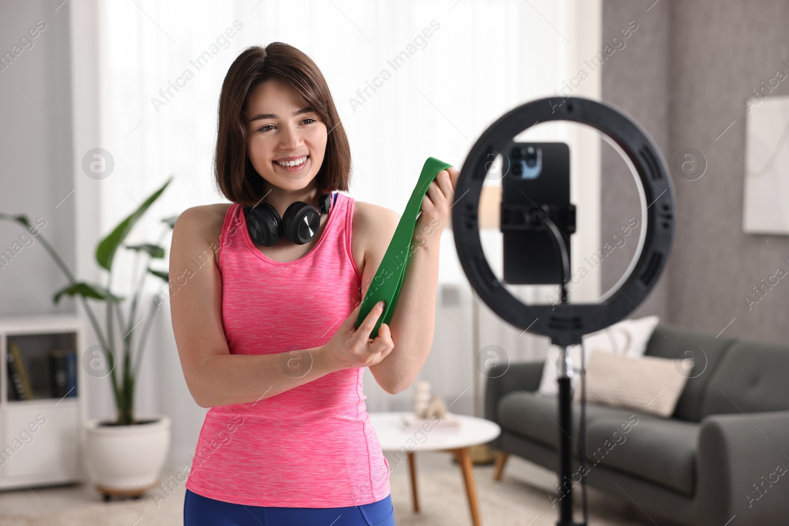 Photo of Happy sports blogger holding resistance band while streaming online fitness lesson with smartphone at home