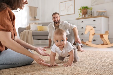 Photo of Happy parents watching their baby crawl on floor at home