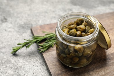 Tasty capers in glass jar and rosemary on grey table, space for text