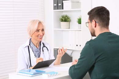 Doctor with pen and clipboard consulting patient at table in clinic
