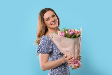 Happy young woman with bouquet of beautiful tulips on light blue background