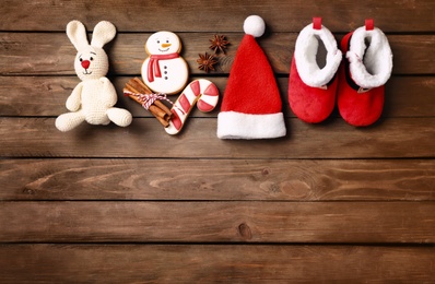 Cute baby booties, small Santa hat, gingerbreads and toy rabbit on wooden background, flat lay. Space for text