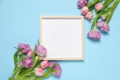 Photo of Empty photo frame and beautiful tulip flowers on light blue background, flat lay. Space for design