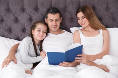 Photo of Happy family reading book with child in bedroom