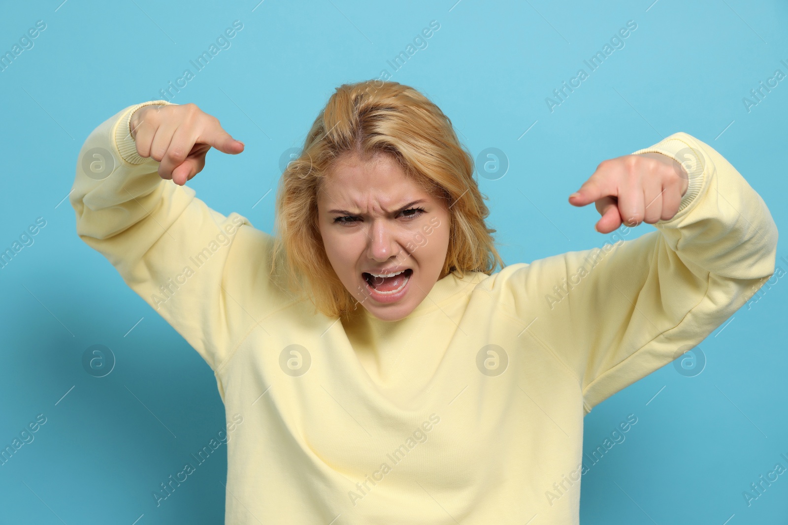 Photo of Aggressive young woman pointing on light blue background