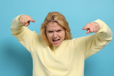 Photo of Aggressive young woman pointing on light blue background