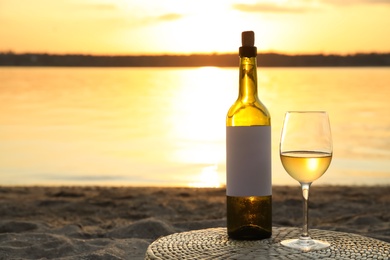 Photo of Bottle and glass of delicious wine on riverside at sunset