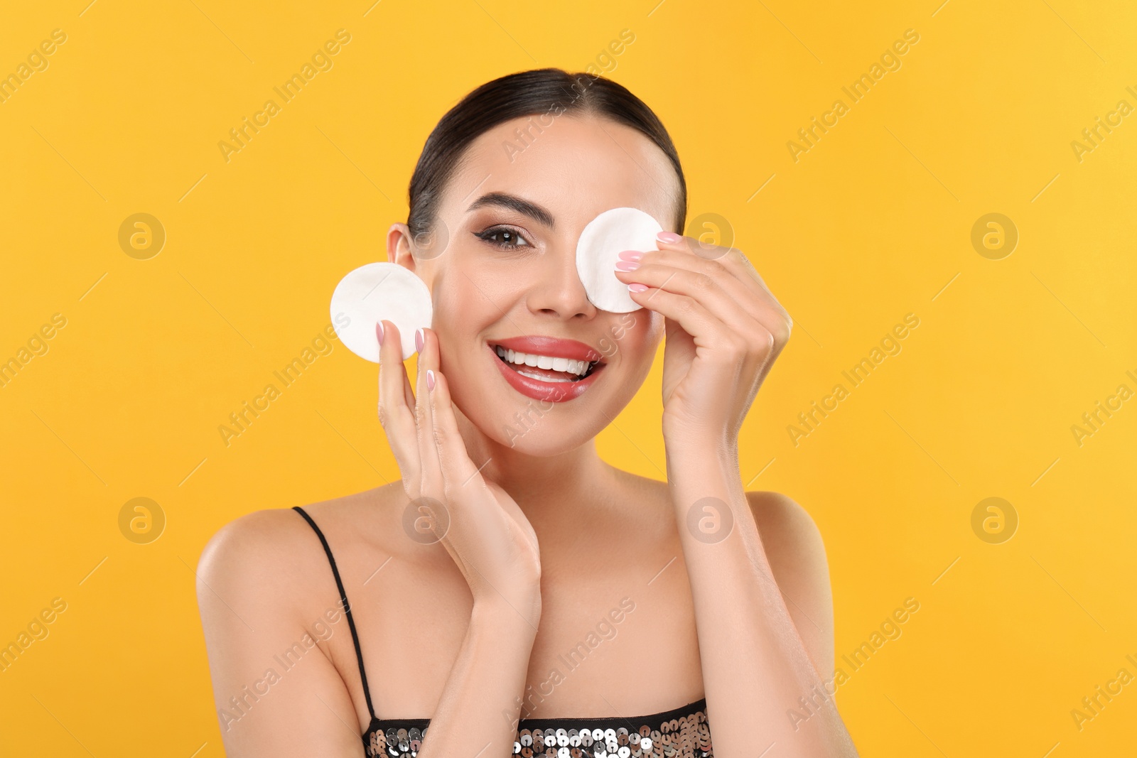 Photo of Beautiful woman removing makeup with cotton pads on orange background