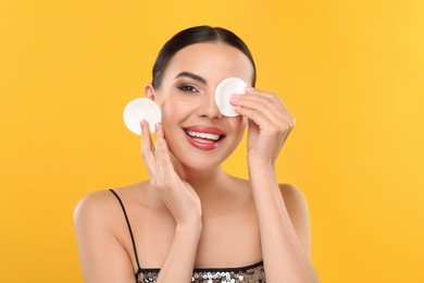 Beautiful woman removing makeup with cotton pads on orange background