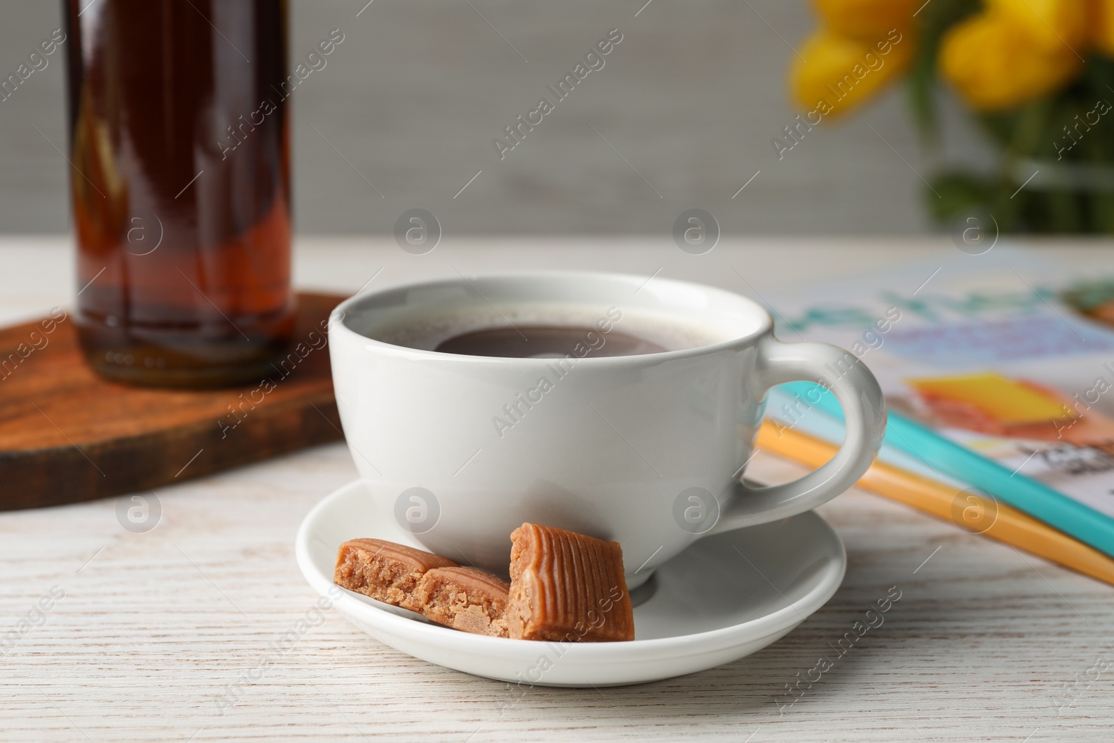 Photo of Cup of aromatic coffee, caramel candies and syrup on white wooden table