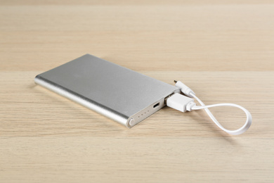 Photo of Modern portable charger with cable on wooden background